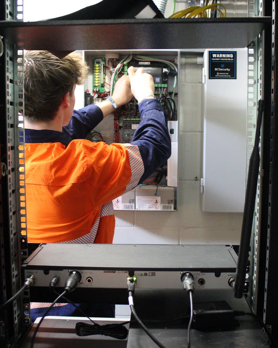 Technician wiring a control panel inside an equipment rack