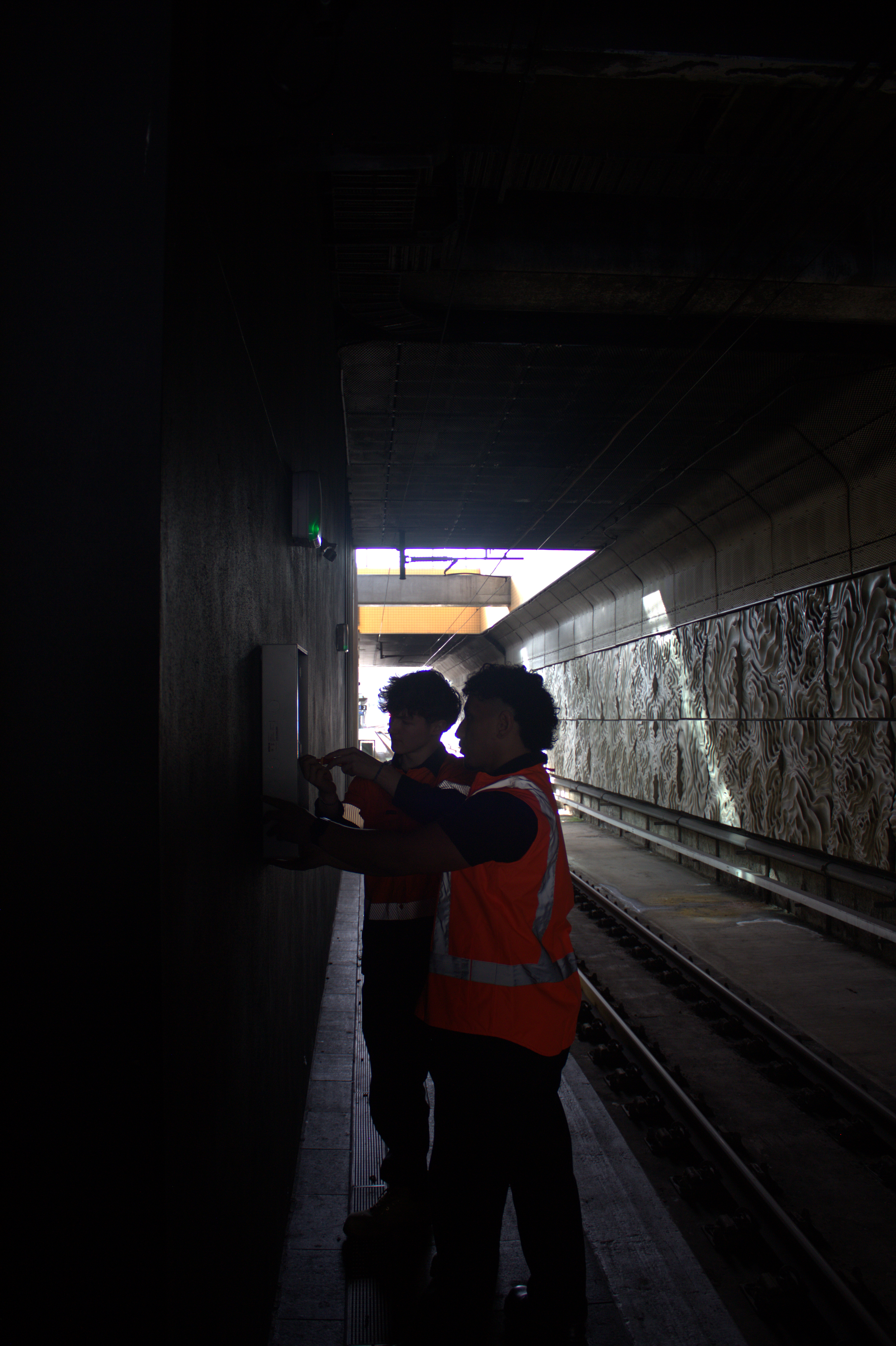 Technicians inspecting wall-mounted security equipment beside a rail platform