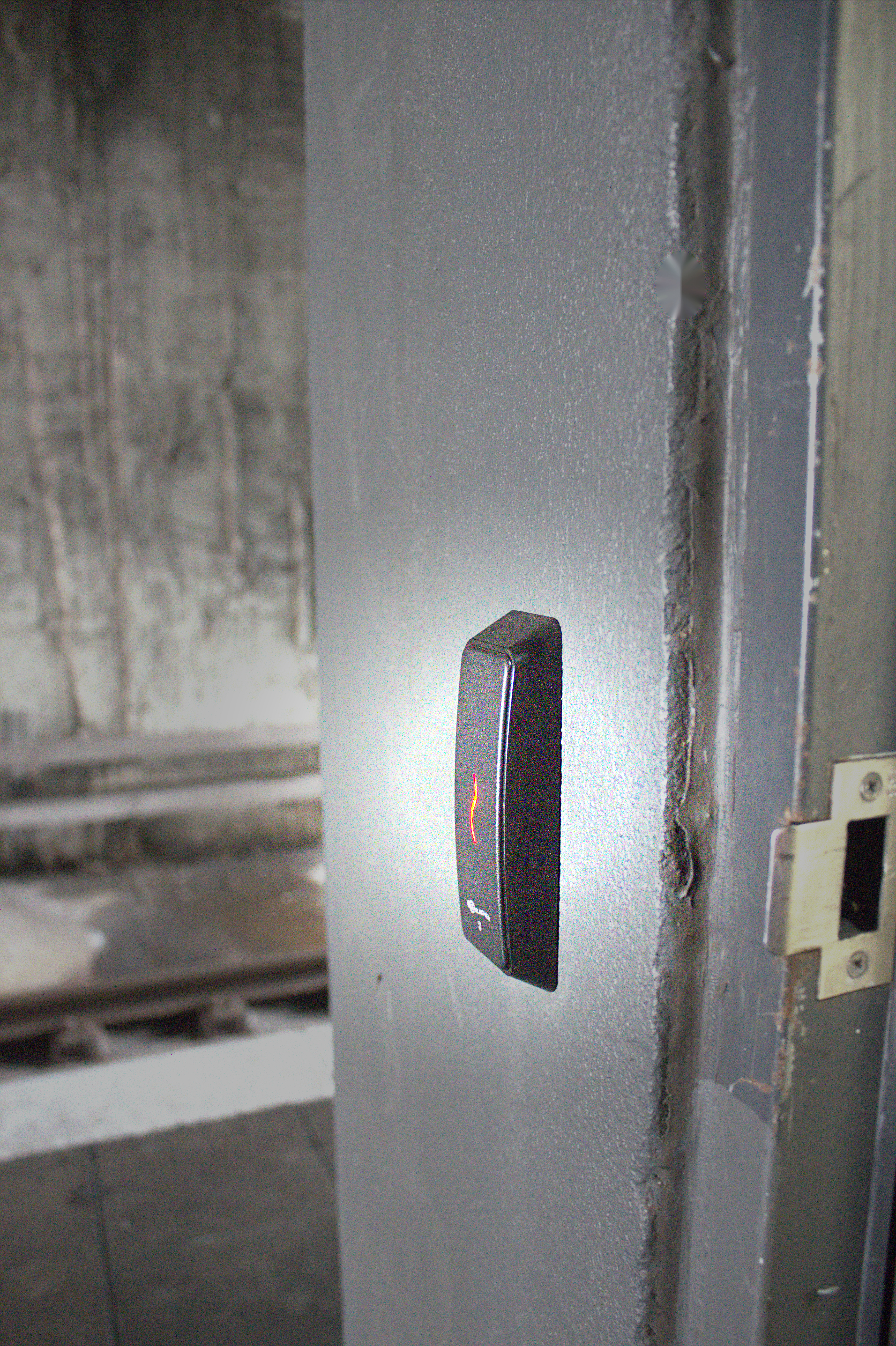 Wall-mounted electronic access reader with red status light beside a door frame